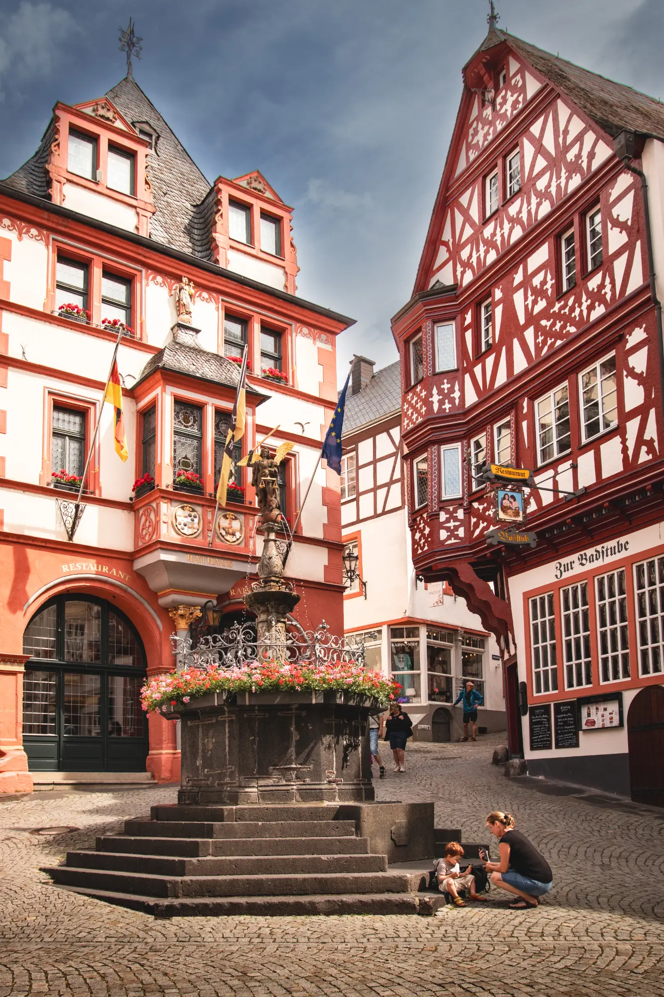 Der historische Marktplatz von Bernkastel-Kues an der Mosel mit Fachwerkhäusern (Rathaus) und dem St.-Michaels-Brunnen in der Mitte, mit einer kleinen Familie im Vordergrund.