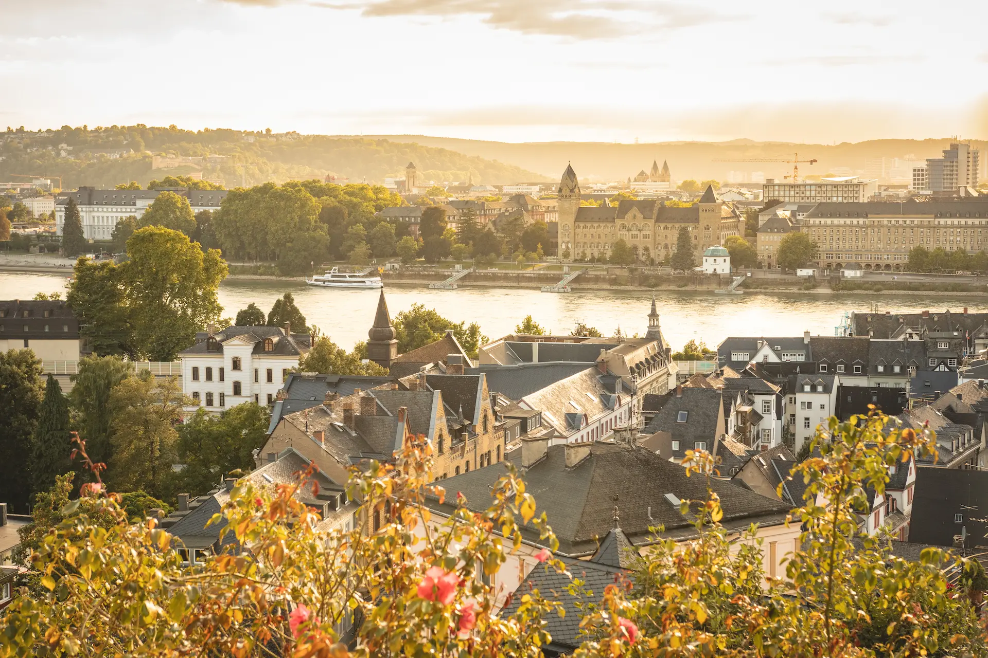 Panoramaaufnahme der Koblenzer Altstadt und des Rheins im warmen Abendlicht, mit Blick auf das Konrad-Adenauer-Ufer und das historische preußische Regierungsgebäude im Hintergrund.