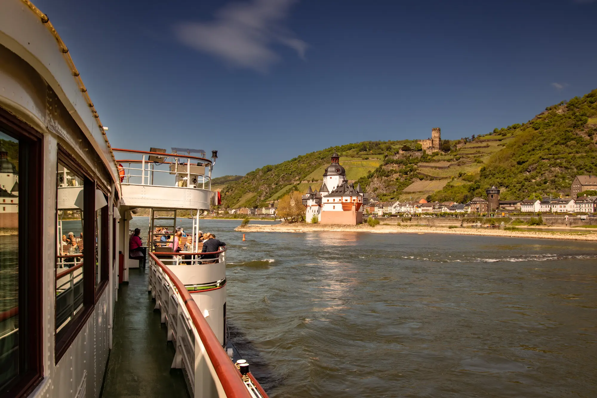 Blick vom Deck eines Passagierschiffs (KD Goethe oder ähnliches) auf die Pfalzgrafenstein Burg in der Mitte des Rheins und Weinberge im UNESCO Welterbe Mittelrheintal.