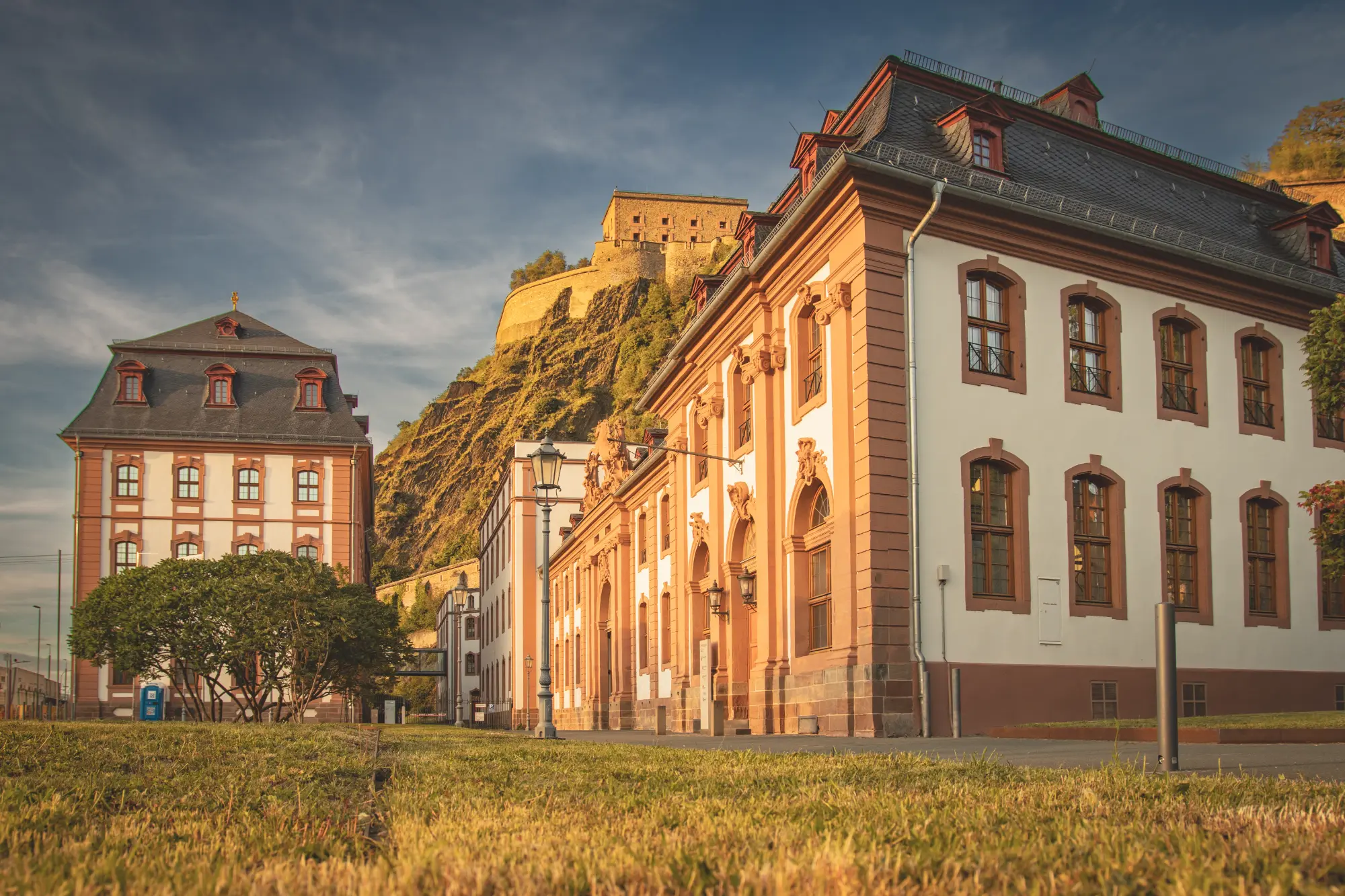 Historische preußische Kaserne oder Dekasterialgebäude am Fuße der steil aufragenden Festung Ehrenbreitstein in Koblenz bei warmem Licht.