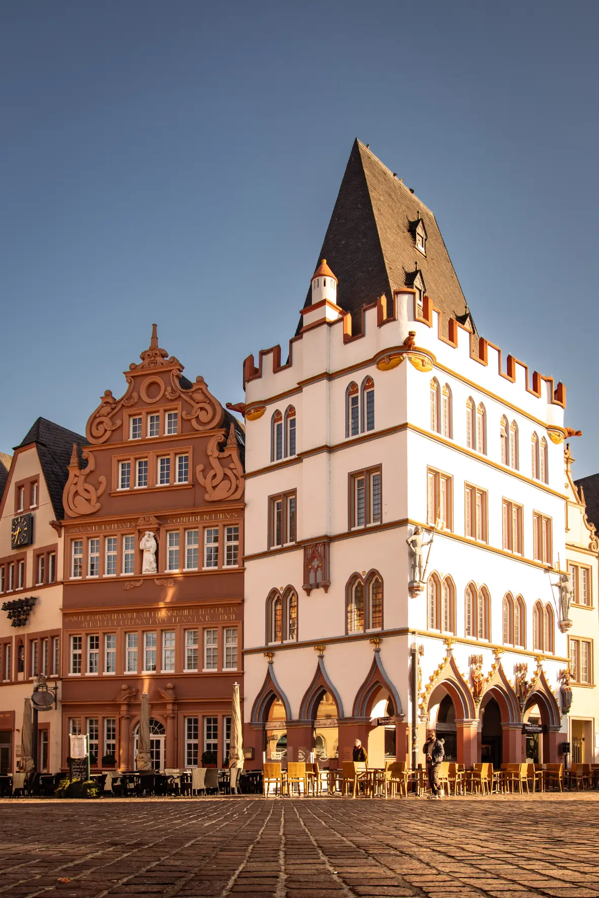 Historische, reich verzierte Fachwerkhäuser im Morgenlicht auf dem Hauptmarkt Trier, darunter das markante Gebäude im Stil der Spätgotik mit einem Turm.