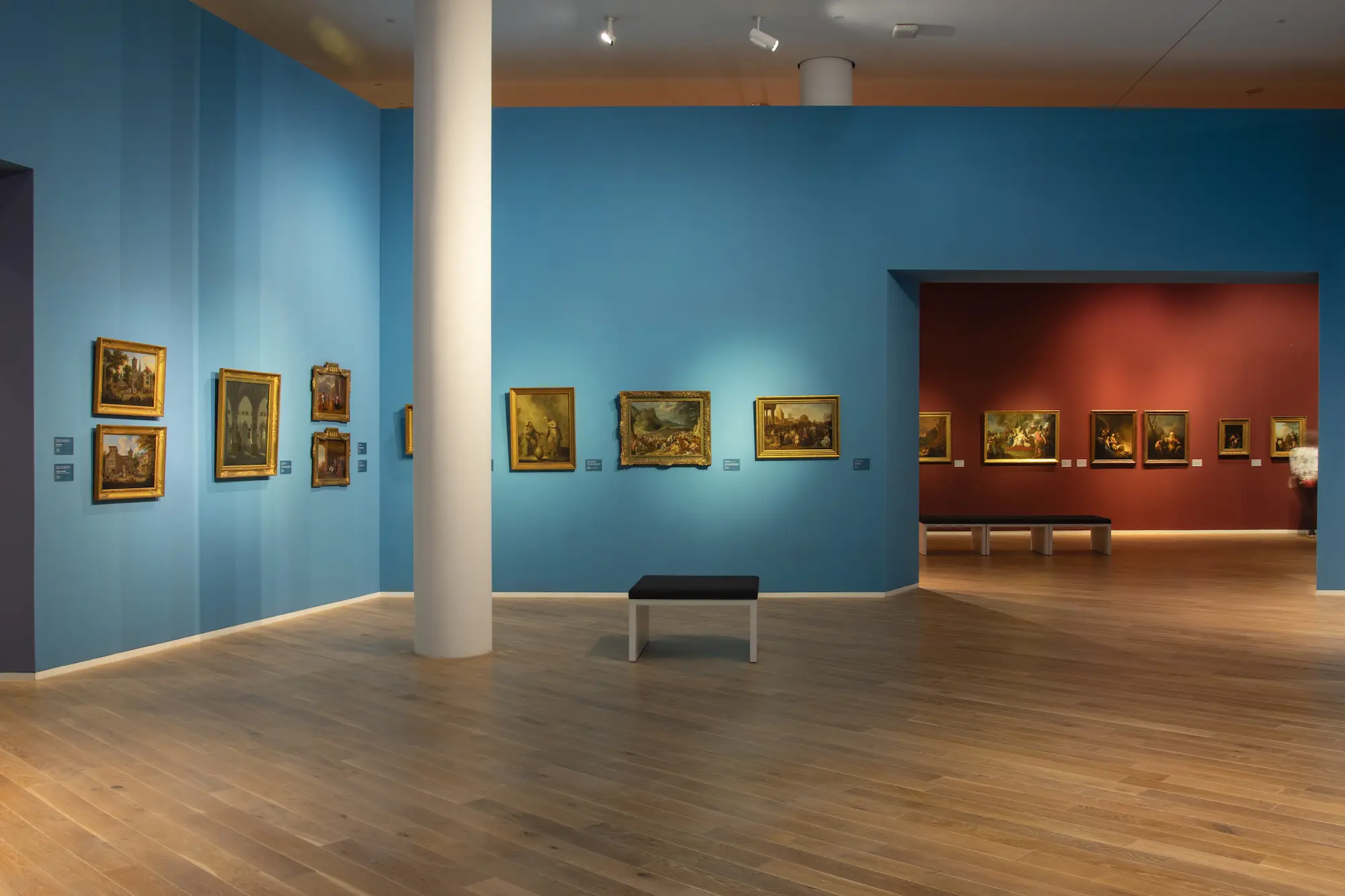 Moderne Museumsräume im Mittelrhein Museum Koblenz mit leuchtend blauen und roten Wänden und vielen gerahmten Ölgemälden, die Landschaften zeigen.
