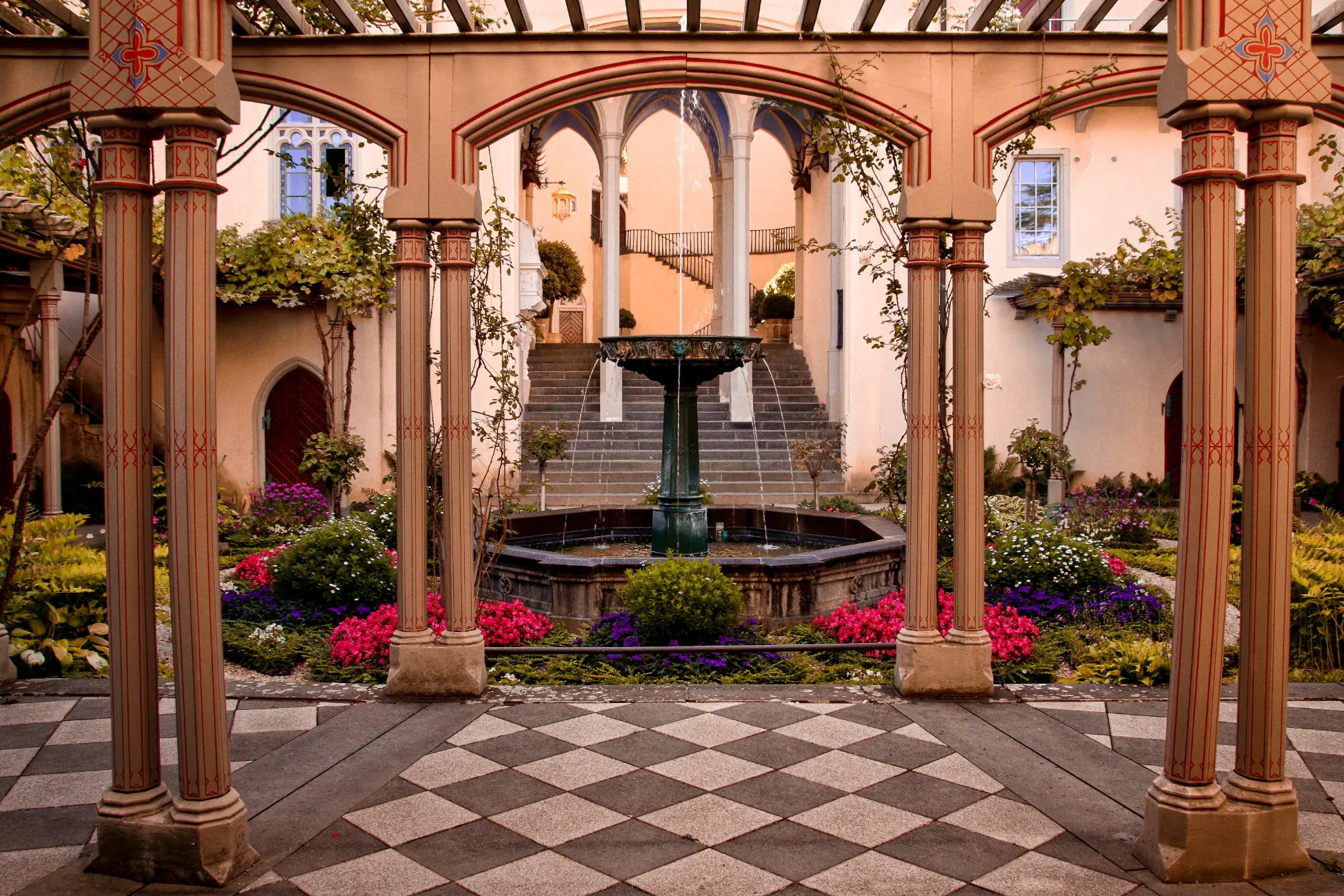 Innenhof des Schloss Stolzenfels mit einem Pergolagarten, Säulen im gotischen Stil, einem Brunnen in der Mitte und einer Treppe im Hintergrund.