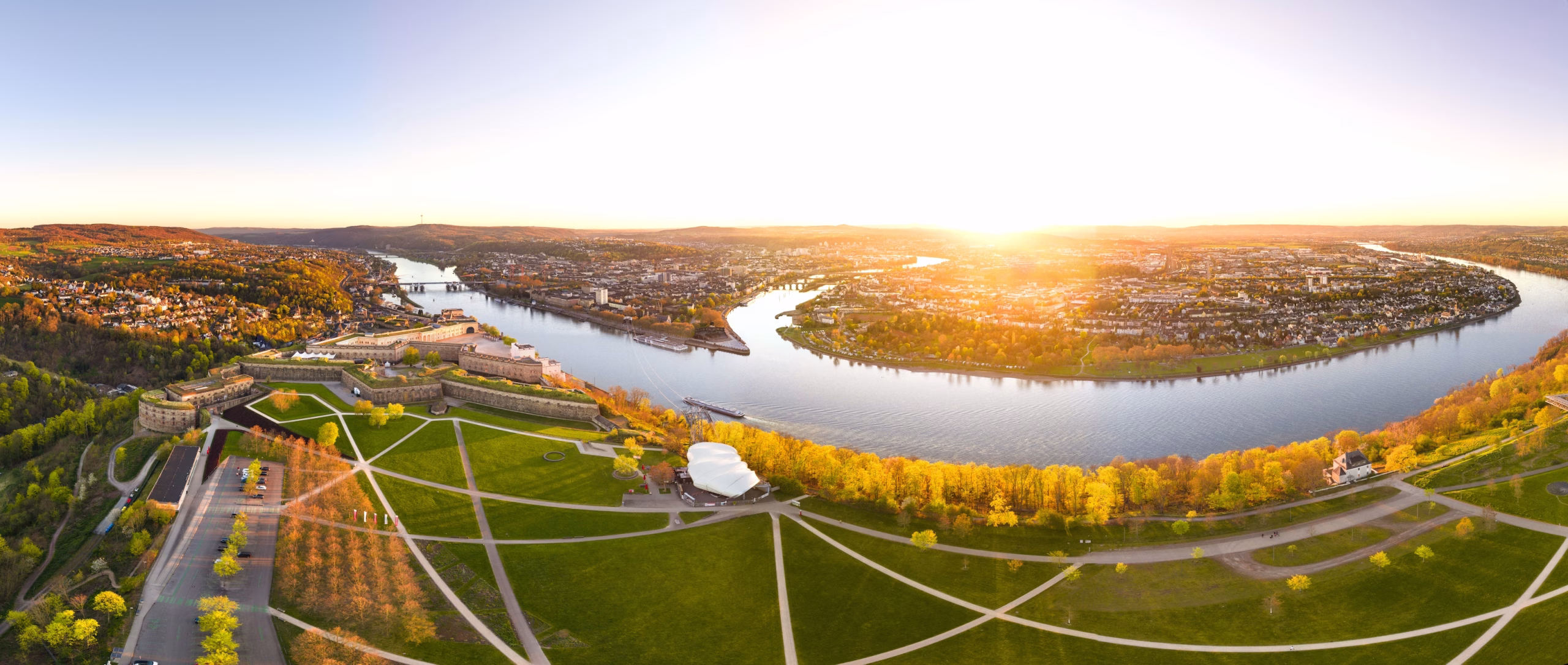 ​Luftaufnahme der Festung Ehrenbreitstein in Koblenz bei Sonnenuntergang mit Blick auf das Deutsche Eck, die Moselmündung in den Rhein und die Seilbahn über dem Fluss.